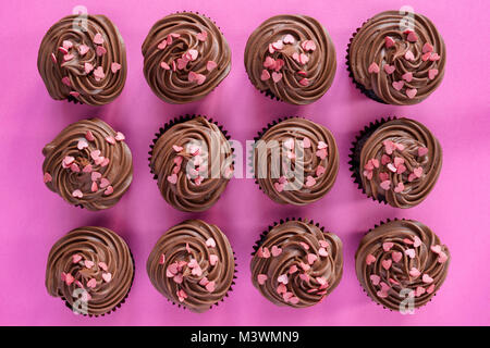 Colourful chocolate cupcakes with heart shaped sprinkles on a pink background. Pattern Stock Photo