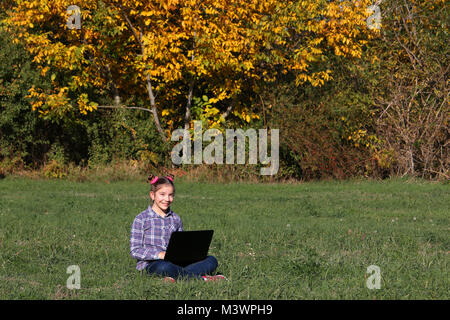 beautiful little girl sitting on grass and playing laptop Stock Photo