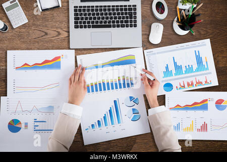 High Angle View Of A Businessperson's Hand Analyzing Graph On Wooden Desk Stock Photo