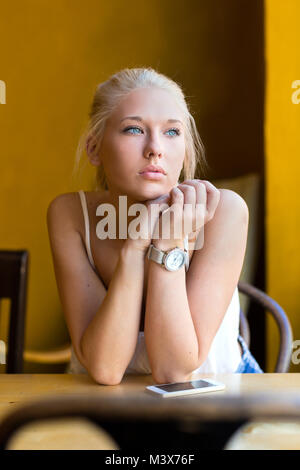 Pensive young woman at cafe looks out the window Stock Photo