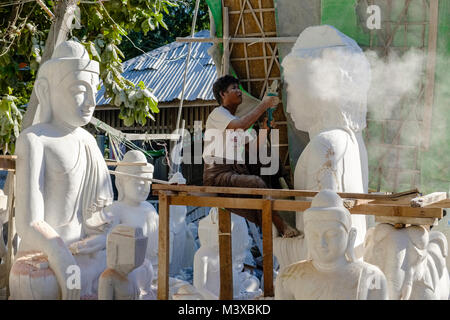 A worker is grinding a Buddha statue from a solid block of white marble Stock Photo