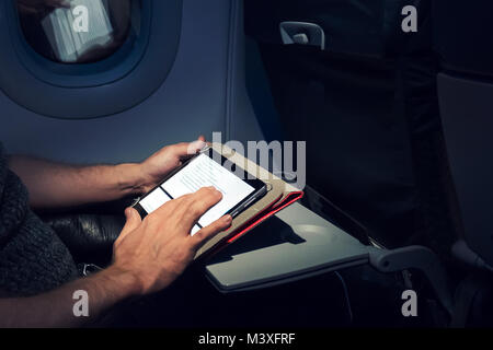 Young man using his tablet on a plane during a flight. This guy's reading an e-book. Electronic book. pastime during the flight on Board the aircraft Stock Photo