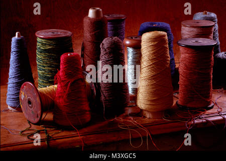 Multiple weaving spools with cotton or wool thread on them.  Vertical color photograph shot in a studio setting with dramatic lighting.  Dark earthy Stock Photo