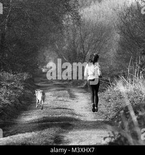 April 2017 - Young woman running with her dog in a country lane in rural Somerset Stock Photo