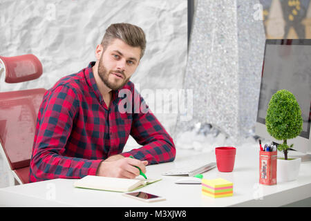 Concentrated on work. Concentrated young beard man working on laptop while sitting at his working place in office Stock Photo