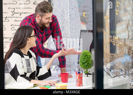 Couple of young designers working at modern office, two coworkers discussing fun project over a laptop, Stock Photo