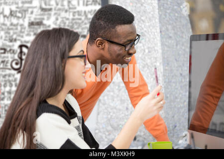 Two diverse work colleagues smiling and writing down notes while sitting together at a table in a modern office Stock Photo