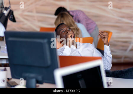 Cheerful black guy is watching at his laptop screen, at his work place, with arms behind the head. Stock Photo
