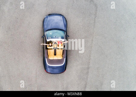Small passenger sports convertible car with soft top down and happy couple of young women enjoying lifestyle and freedom in aerial top down view. Stock Photo
