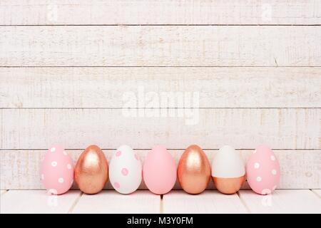 Row of Easter eggs on a white wood background. Rose gold, soft pink and white colors. Stock Photo
