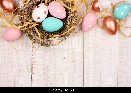 Springtime nest with pink, rose gold and turquoise painted Easter Eggs. Top border against a rustic white wood background. Stock Photo