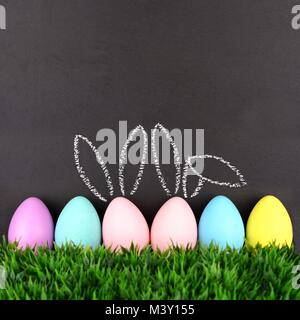 Row of Easter eggs in grass against a chalkboard background. Two with hand drawn Easter Bunny ears. Stock Photo