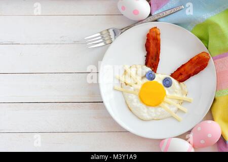 Easter breakfast with cute bunny face made of egg and bacon. Top view scene with decor over a white wood background. Stock Photo