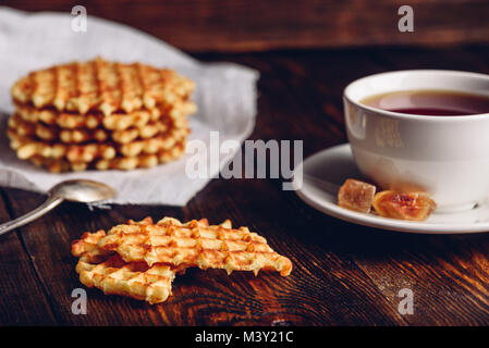 Breakfast with White Cup of Tea with Waffles Stack on Napkin and Pieces of Waffle on Wooden Surface. Stock Photo
