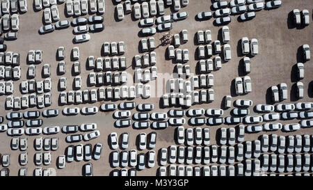 New cars covered in protective white sheets parked in a holding platform - Aerial footage Stock Photo
