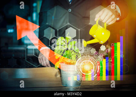 Hand of businessman watering on plant with technology and business icons, red arrow, graph. Stock Photo