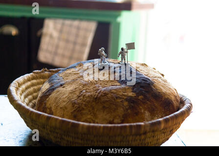two toy astronaut figures, one with a flag, stand on top of a freshly baked sourdough loaf resembling a moon landing, in a french kitchen Stock Photo