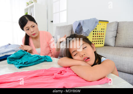pretty elegant housewife finding little daughter sleeping feeling helpless when they folding clothing together in living room. Stock Photo