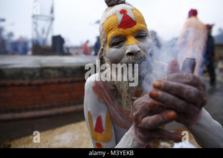 Kathmandu, Nepal. 13th Feb, 2018. A Sadhu or holy man smokes a marijuana chillum during Maha Shivaratri festival inside Pashupatinath Temple in Kathmandu, Nepal on Tuesday, February 13, 2018. Thousands of sadhus from India and Nepal come to celebrate the festival of Maha Shivaratri by smoking marijuana, smearing their bodies with ash and offering prayers devoted to the Hindu Deity Lord Shiva. Credit: Skanda Gautam/ZUMA Wire/Alamy Live News Stock Photo