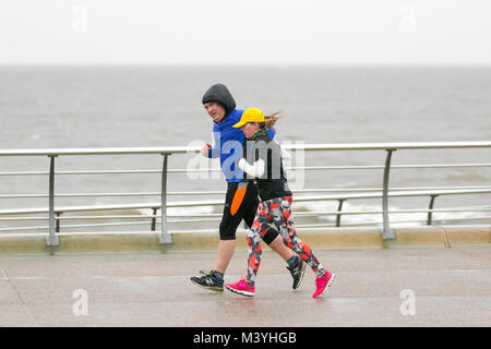 Blackpool, Lancashire. 13th Feb, 2018. UK Weather: Cold, wet and blustery start to the day, as joggers take light exercise,  on the seafront promenade. Normally a haven for half-term visitors this years mid-term break is without the Showzam event which used to wow the crowds in previous years. Torrential  downpours  make  it  difficult  for visitor & tourists  who  struggle  with  the  strong  gusts,  blustery  and  windy  conditions.  The  forecast  is  for  continuing  persistent  and  often  heavy  rain  slowly  moving  eastwards  with  strong  winds. Credit: MediaWorldImages/AlamyLiveNews. Stock Photo