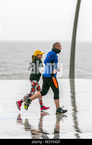 Runners in Blackpool, Lancashire. 13th Feb, 2018. UK Weather: Cold, wet and blustery start to the day, as two joggers take light exercise,  on the seafront promenade. Normally a haven for visitors this years mid-term break is without the Showzam event which used to wow the crowds in previous years. Torrential downpours make it difficult for visitor & tourists who struggle with the strong gusts, blustery and windy conditions. The forecast is for continuing persistent and often heavy rain slowly moving eastwards with strong winds Stock Photo