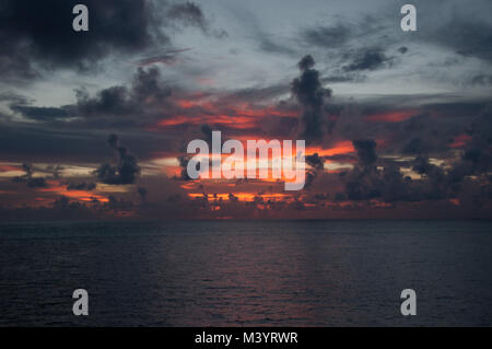 Incredible colorful sunset on the ocean, gray and fiery flare in the sky among the clouds, pink patches of light on the waves. Stock Photo