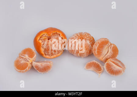 Three peeled orange mandarin beads and individual slices with white veins lie in a semicircle on a light grayish background. Stock Photo