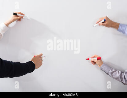 Close-up Of Business People's Hands Holding Different Marker Writing On Whiteboard Stock Photo