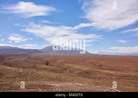 Arid landscape of the Atacama desert with the Andes Mountain range in the background. A clear blue sky with clouds hangs above. Stock Photo