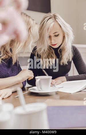 Two young women discussing documents and drinking tea at meeting in conference room Stock Photo