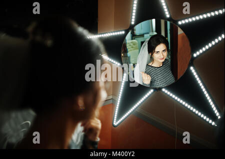 Fabulous bride looking at star-shaped mirror in makeup salon before the wedding. Stock Photo