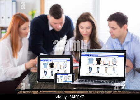 Online Shopping Screen On Modern Electronic Devices With Colleagues Working At Workplace Stock Photo