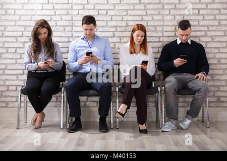 Business People Sitting On Chair Using Smart Phone In Office Stock Photo