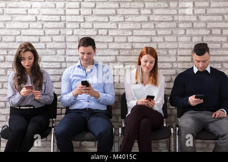 Young Business People Sitting On Chair Using Cell Phone Against Brick Wall Stock Photo