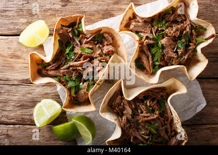 Mexican barbacoa with beef, lime and greens close-up on paper on table. horizontal top view from above Stock Photo