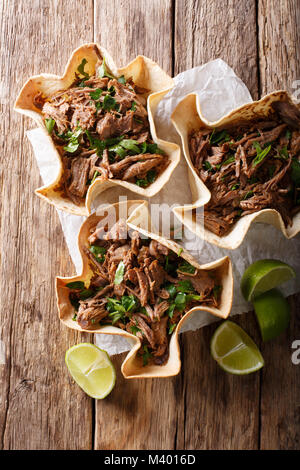 Mexican barbacoa with beef, lime and greens close-up on paper on table. Vertical top view from above Stock Photo