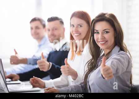 Smiling Woman With Her Colleagues Showing Thumb Up Sign In Office Stock Photo