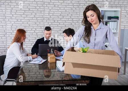 Young Businesswoman Leaving Office After She Was Fired With Her Colleagues In Background Stock Photo