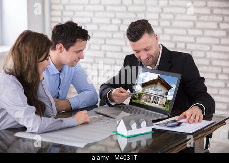 Male Architect Showing House Model On Laptop To Couple In Office Stock Photo