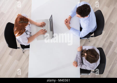 Elevated View Of Doctor Sitting With Couple Patient Using Laptop On Desk Stock Photo