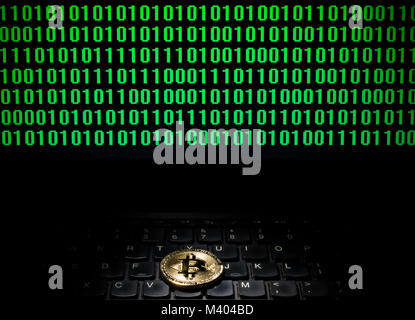 bitcoin on a laptop with a sceen of binary code Stock Photo