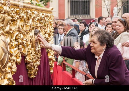 Old woman touching the head of an angel carved in the float of Christ of the brotherhood of 'la Paz'. Stock Photo