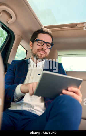 Smiling businessman using a tablet during his morning commute Stock Photo