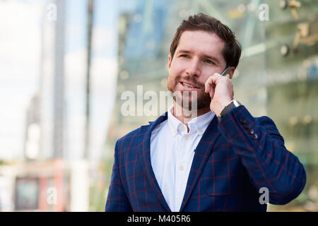 Smiling businessman standing in the city talking on a cellphone Stock Photo