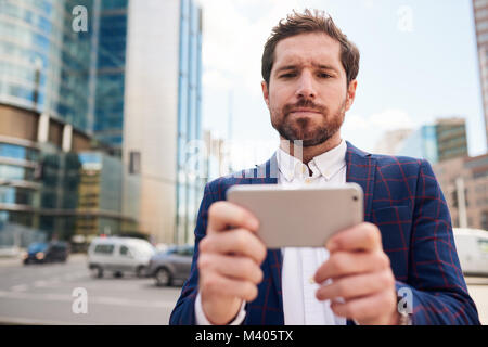 Young businessman standing on a city street using his smartphone   Stock Photo