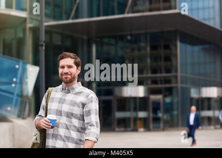 Smiling young man standing in the city drinking coffee   Stock Photo