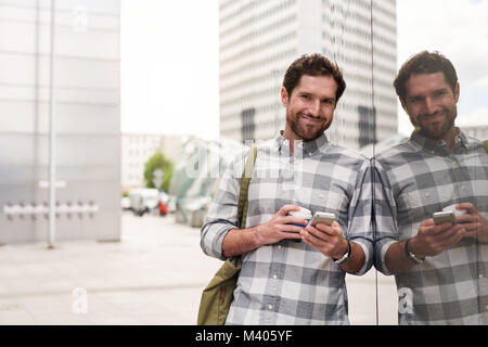 Smiling young man standing in the city using his cellphone Stock Photo