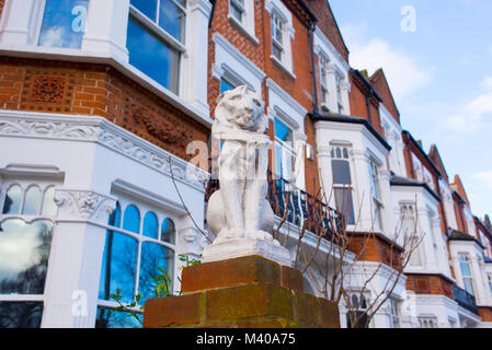 Statue of a lion in white stone in front of a row of restored luxury Victorian houses in red bricks and white finishing on a local street in London, U Stock Photo