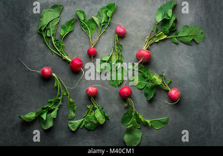 Fresh Raw Ripe Red Radishes with Green Leaves Scattered on Dark Concrete Stone Background. Top View Flat Lay. Minimalist Style. Creative Image Templat Stock Photo