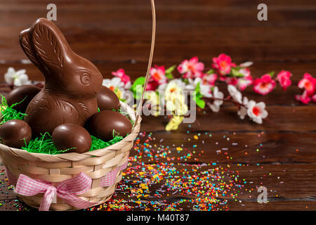 Beautiful Easter composition with chocolate bunny and eggs in a wicker basket with a bow, colored powder for cakes on old brown wooden background Stock Photo